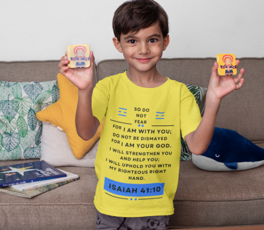 Child wearing a yellow t-shirt with a biblical verse, holding two small colorful items, sitting on a couch.