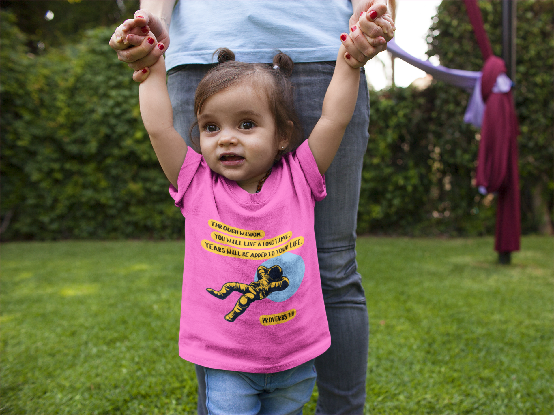 Child wearing a pink shirt with a cartoon character, standing outdoors on grass.