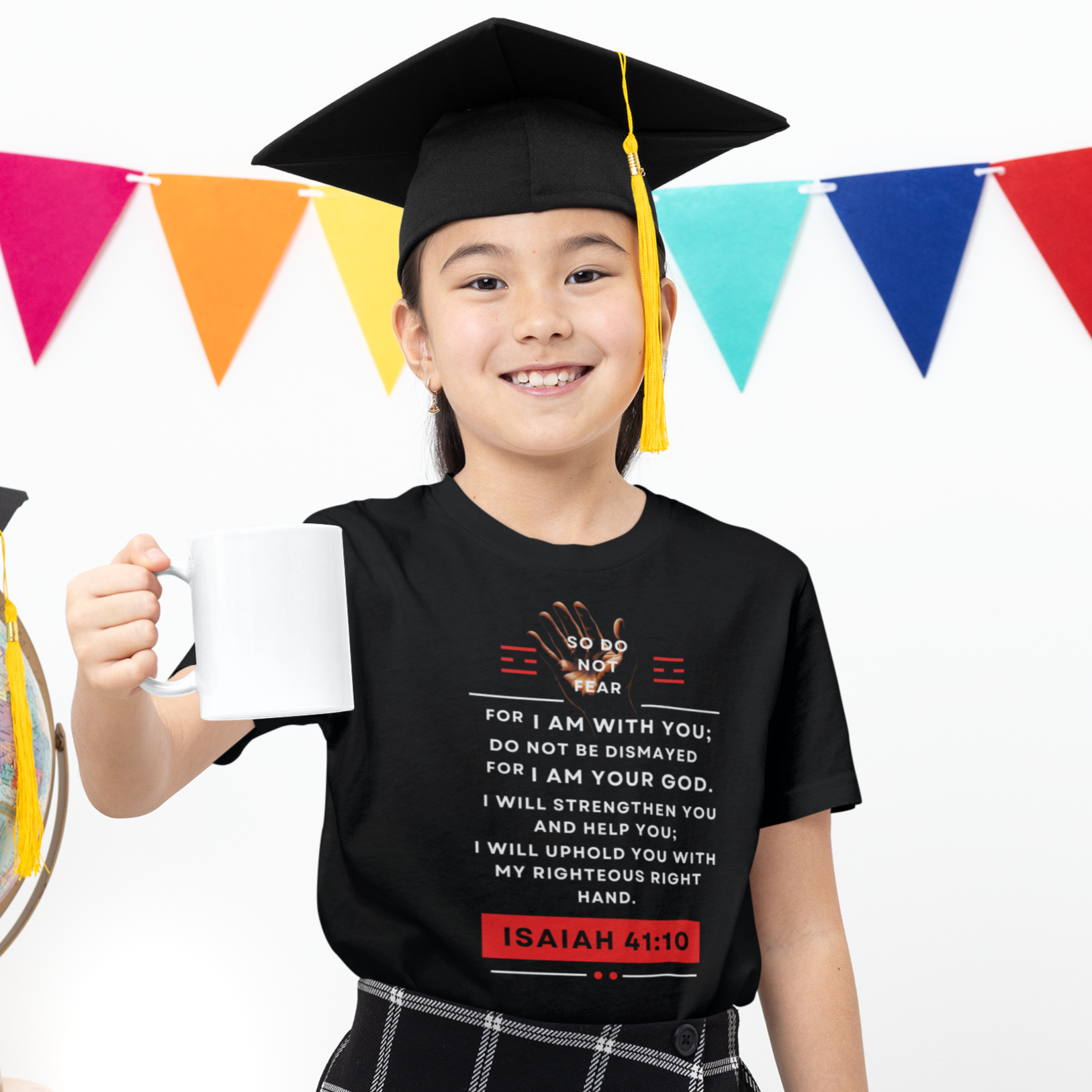 Child in graduation cap and gown holding a mug with colorful flags in the background