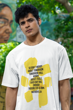 Man wearing a white t-shirt with a yellow graphic and text, standing in front of a mural.