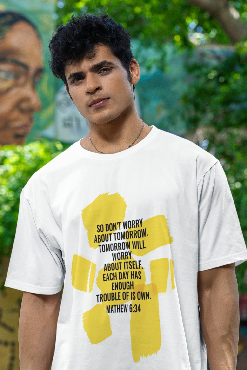 Man wearing a white t-shirt with a yellow graphic and text, standing in front of a mural.