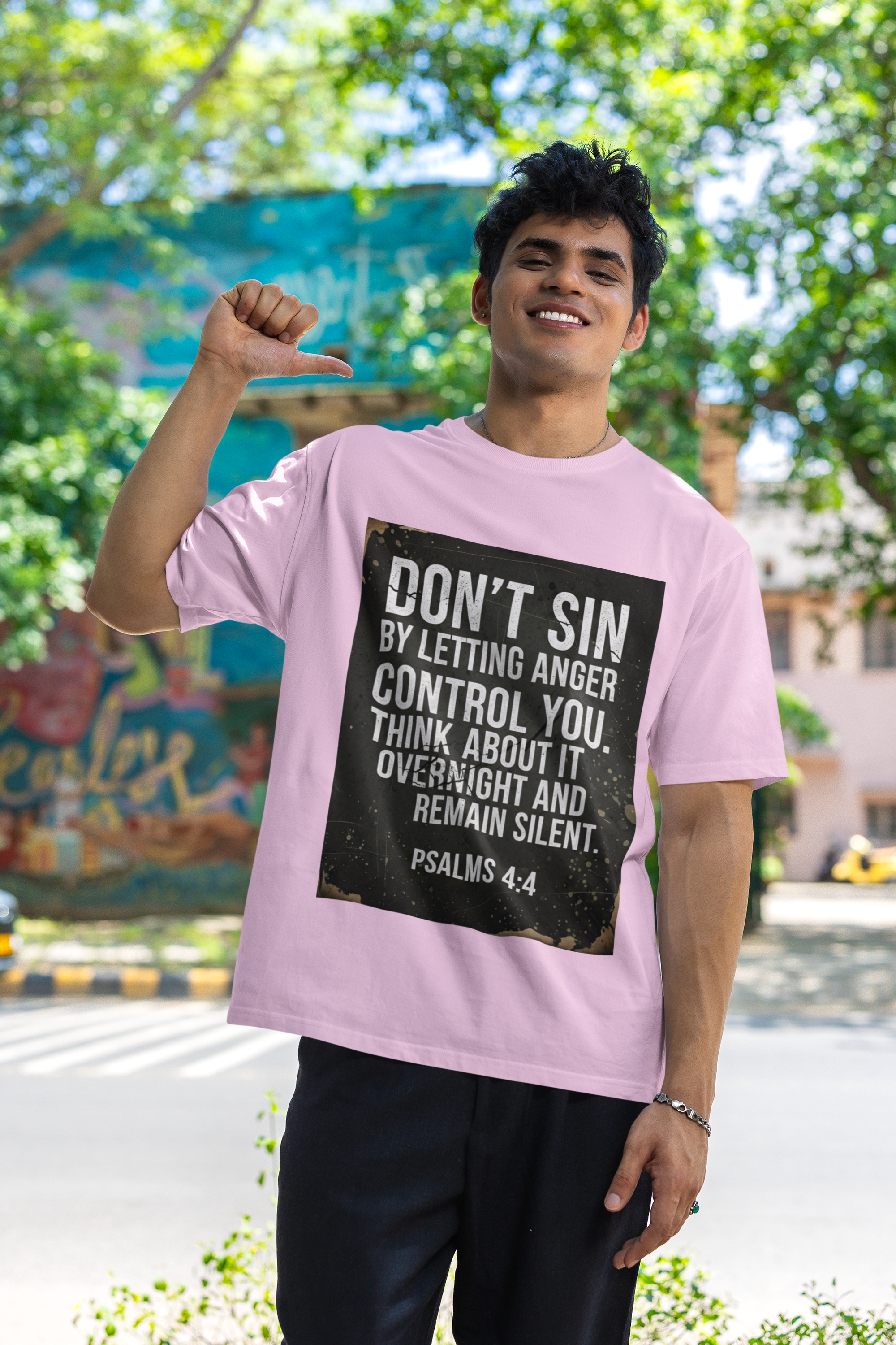 Person wearing a pink t-shirt with a motivational quote, standing outdoors with trees and buildings in the background.
