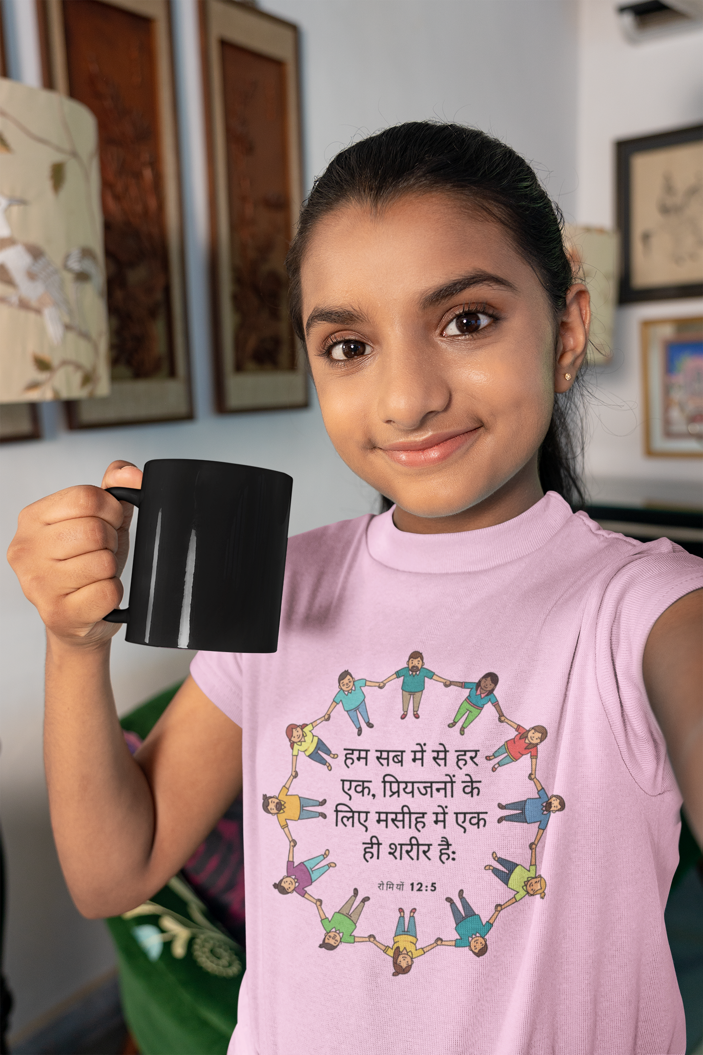 Young girl holding a black mug and wearing a pink sleeveless shirt with a colorful design and text.