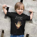 Child wearing a black t-shirt with a hand illustration and text, standing against a stone wall.