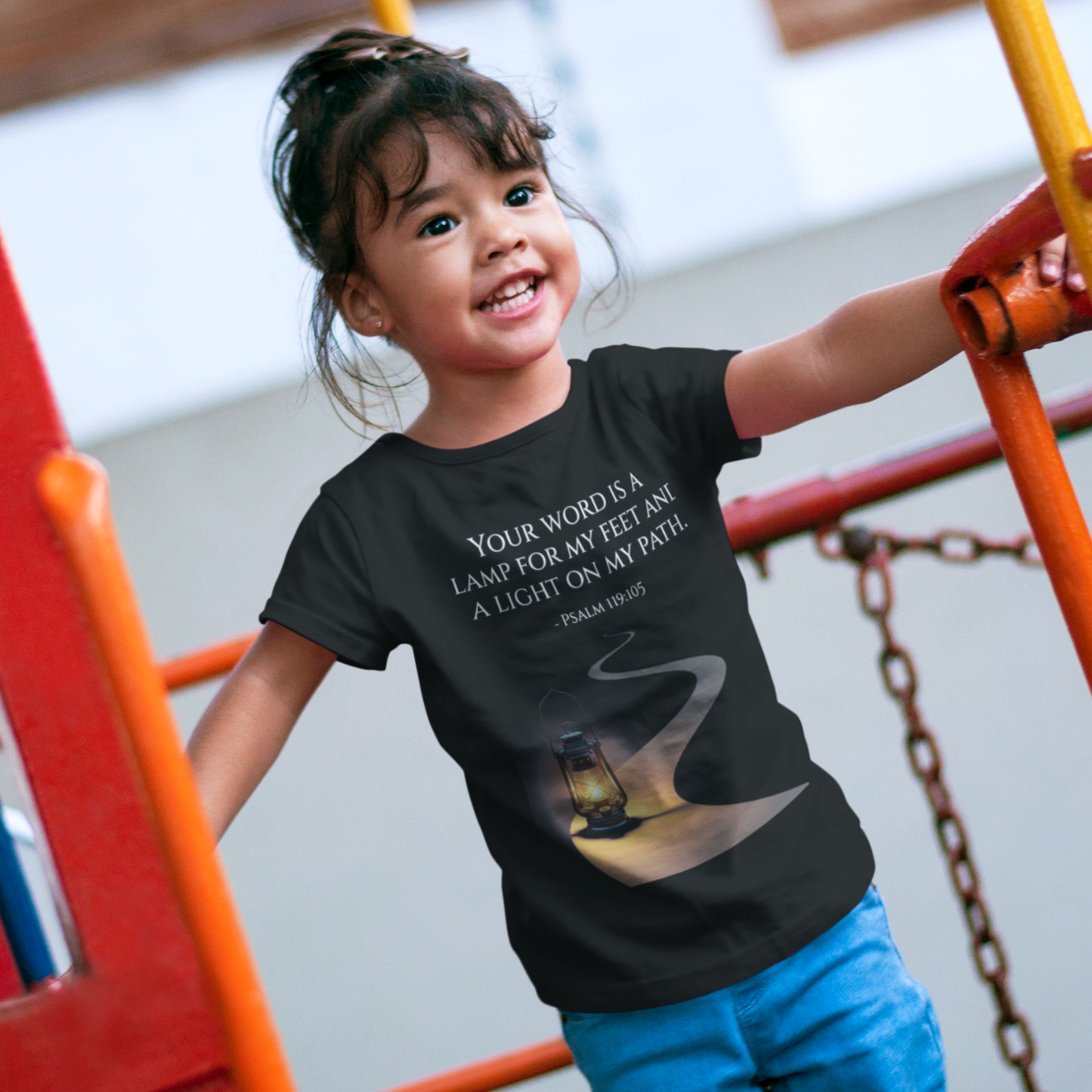 Child wearing a black t-shirt with text and a graphic on a playground.