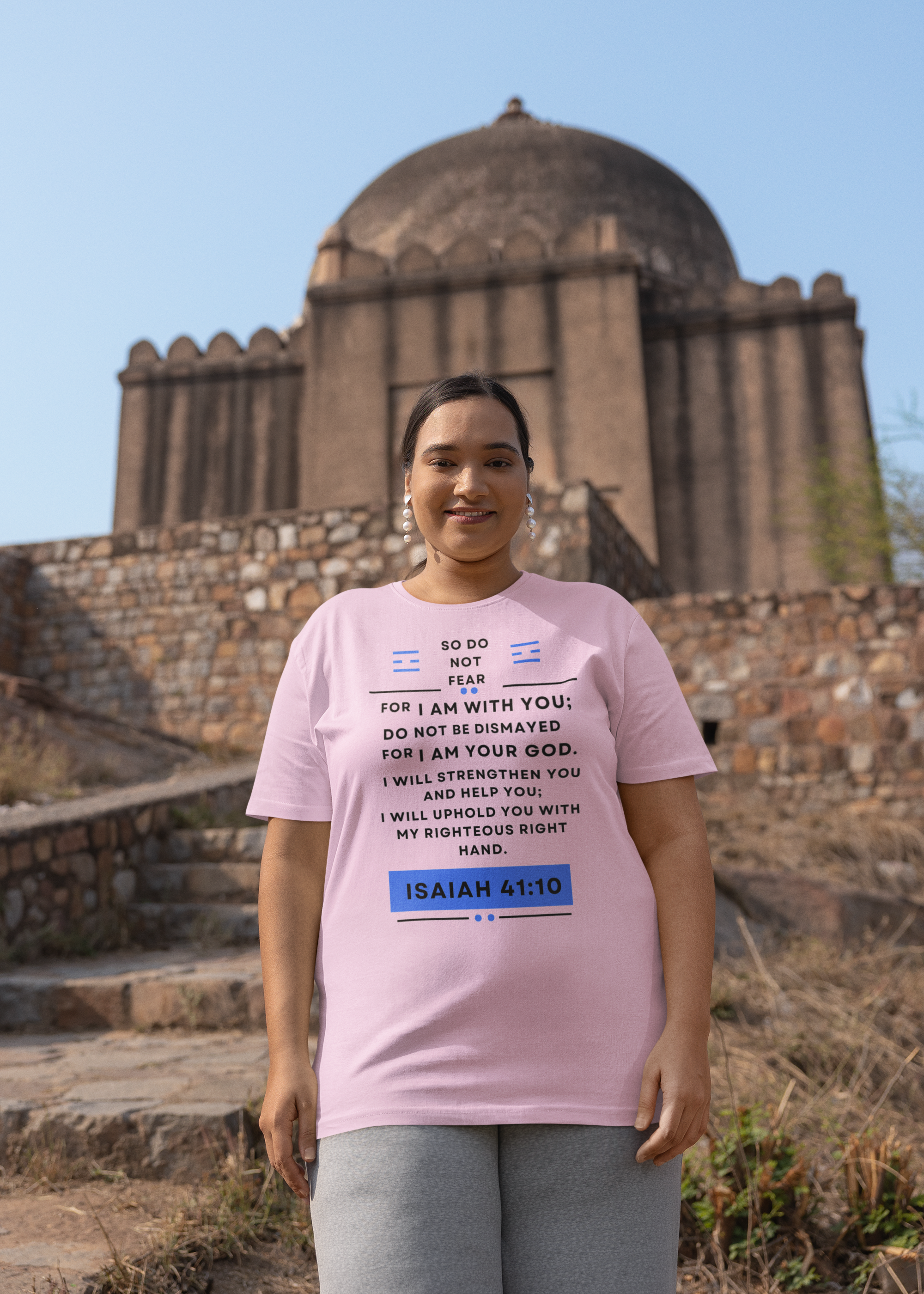 Person wearing a pink t-shirt with text and a blue box in front of an architectural structure.
