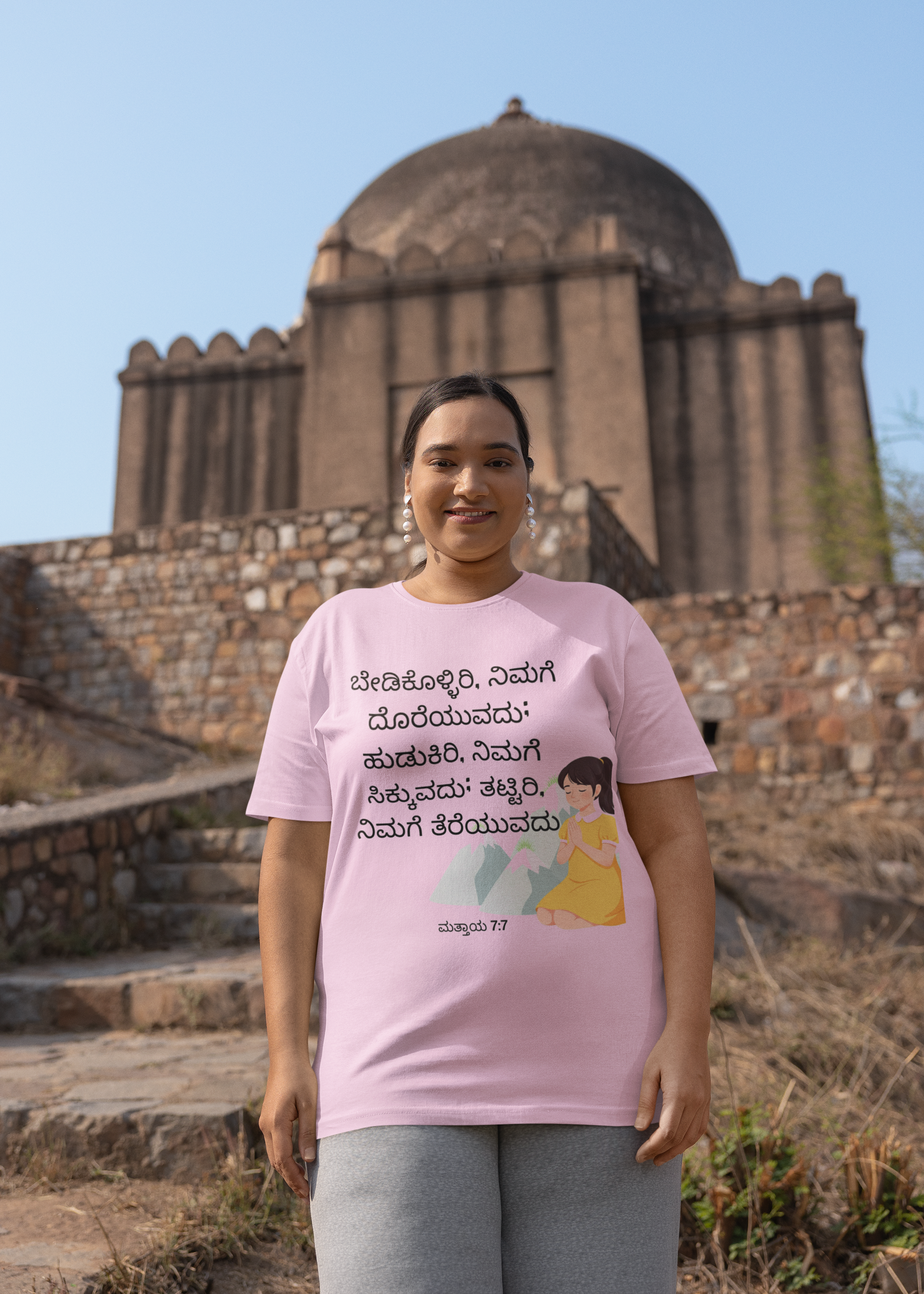 Person wearing a pink t-shirt with text and graphics in front of an architectural structure.