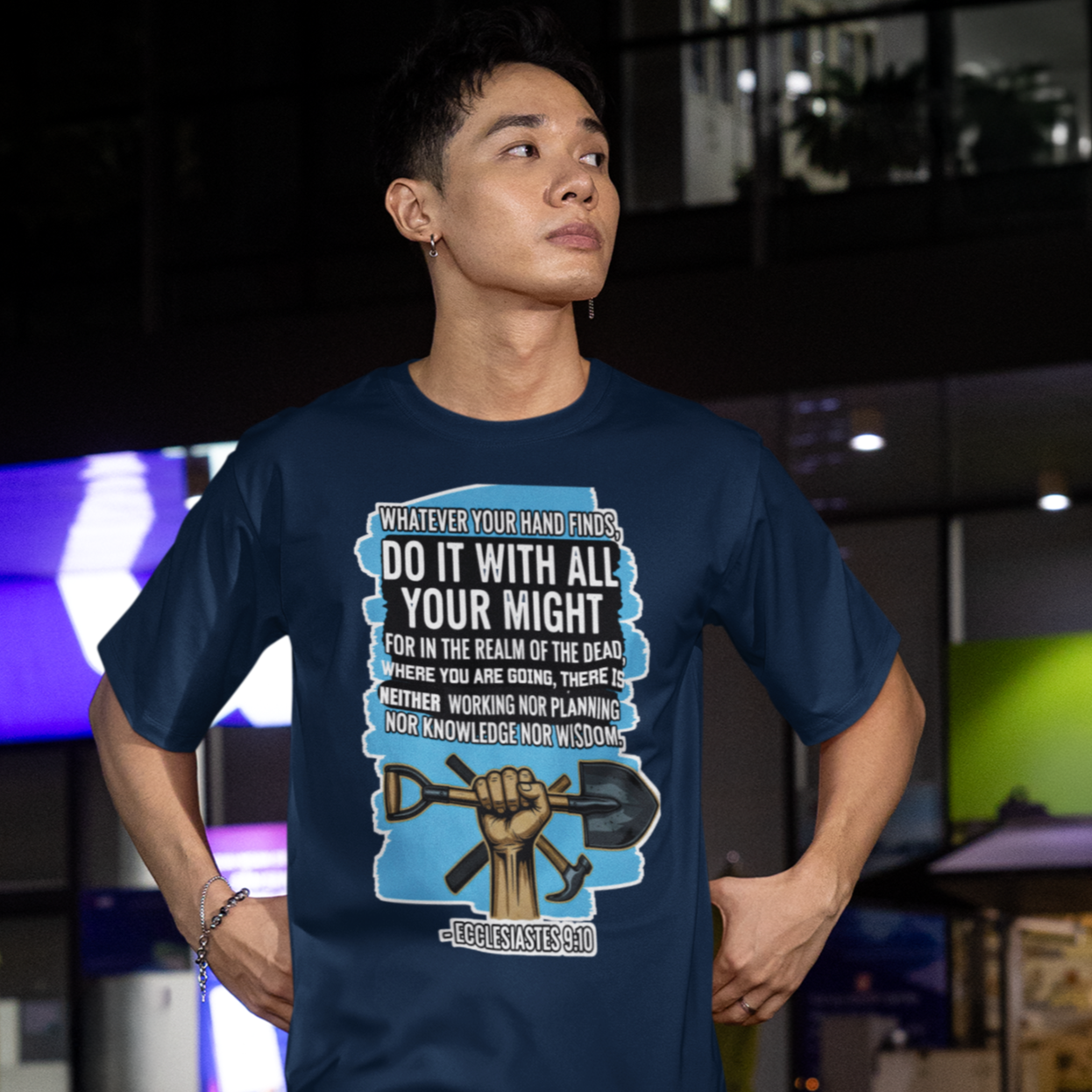Person wearing a blue t-shirt with graphic design and text, standing outdoors at night.