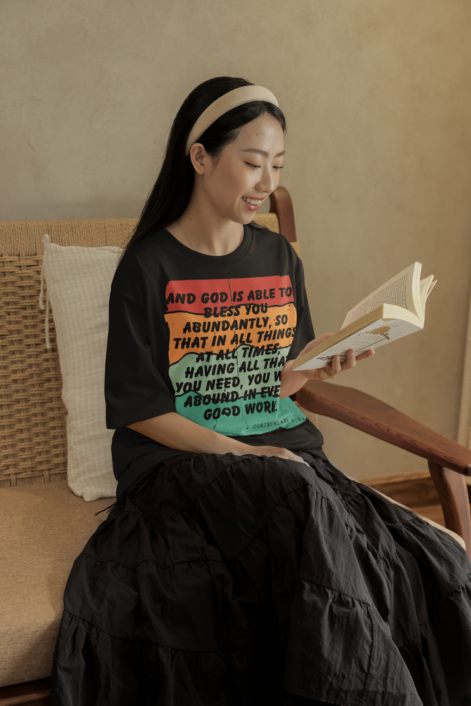 Woman sitting on a couch reading a book, wearing a black t-shirt with colorful text.