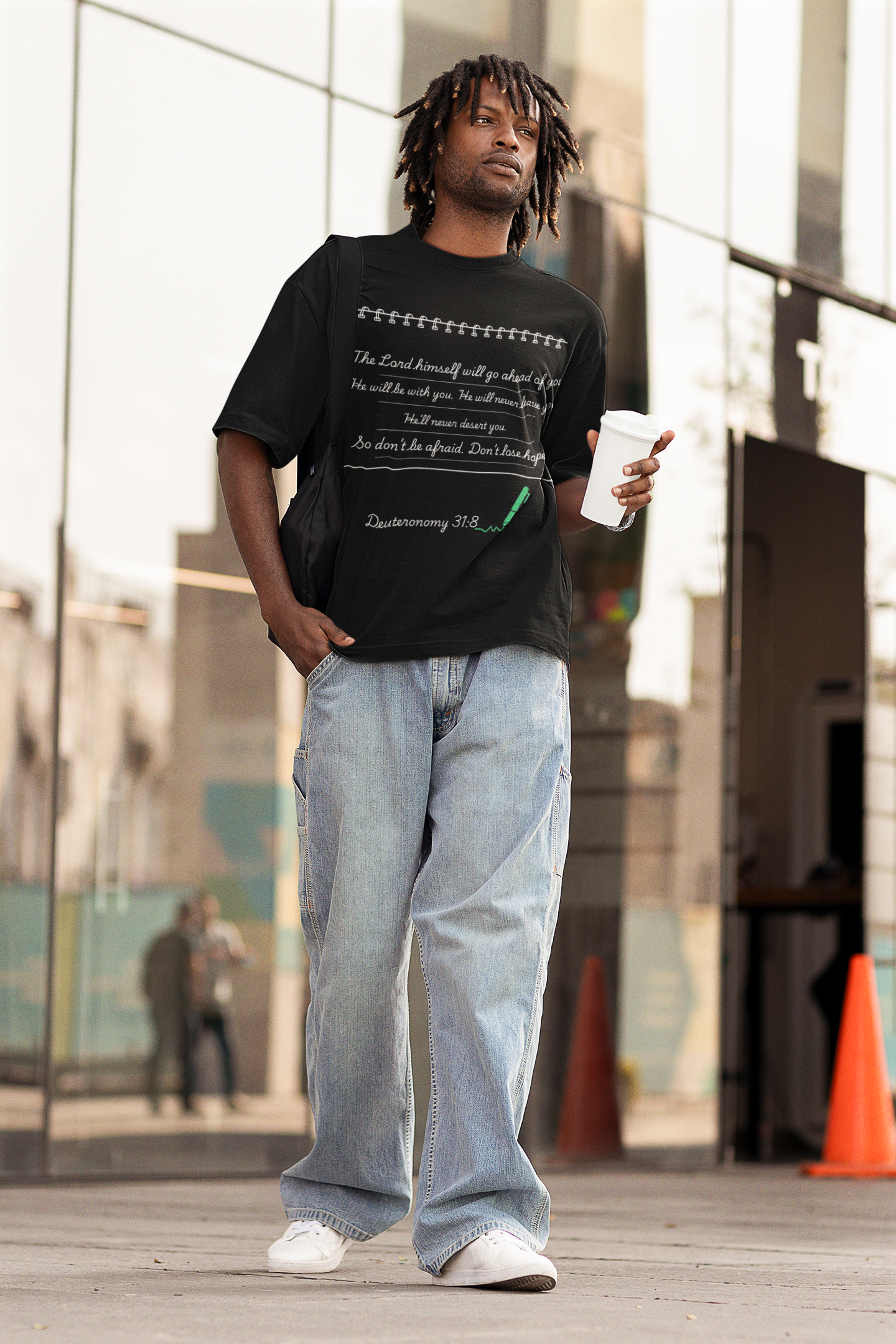 Man wearing a black t-shirt with text and light blue jeans standing outdoors.