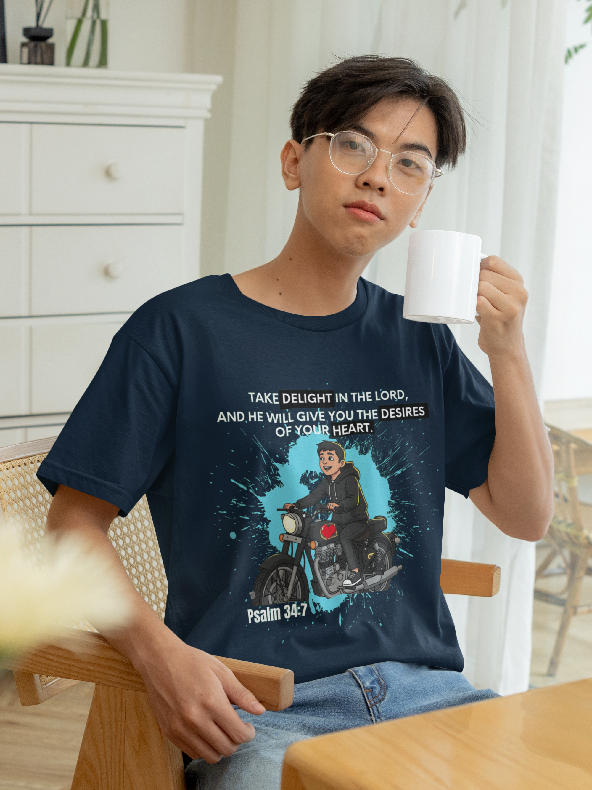 Person wearing a t-shirt with a graphic design and text, holding a mug indoors.