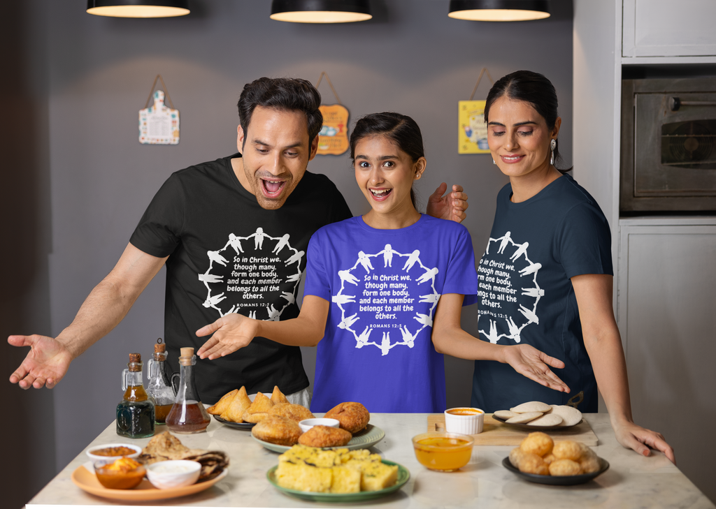 Three people wearing t-shirts with a design, standing around a table with food items.