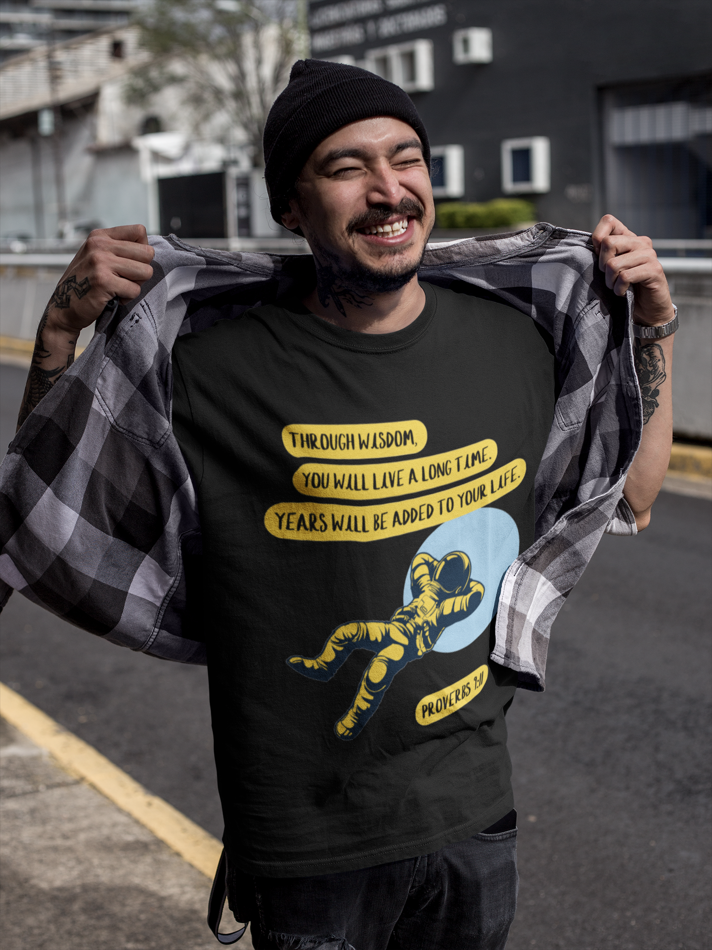Man wearing a black t-shirt with graphic design and text, holding a checkered shirt.
