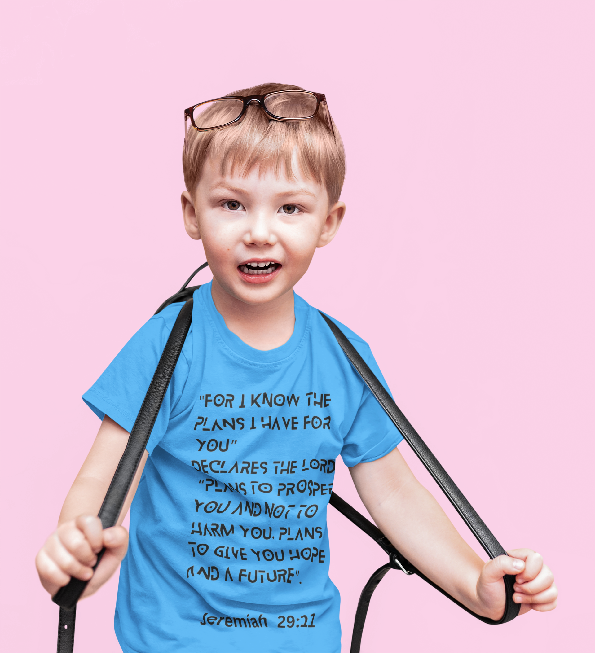 Child wearing a blue t-shirt with a quote, holding straps against a pink background