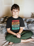 Young boy sitting on a bed wearing a black t-shirt with colorful text.