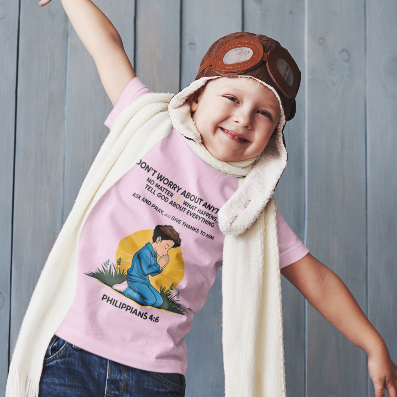 Child wearing a pink t-shirt with a graphic design, blue jeans, and a white scarf against a wooden background.