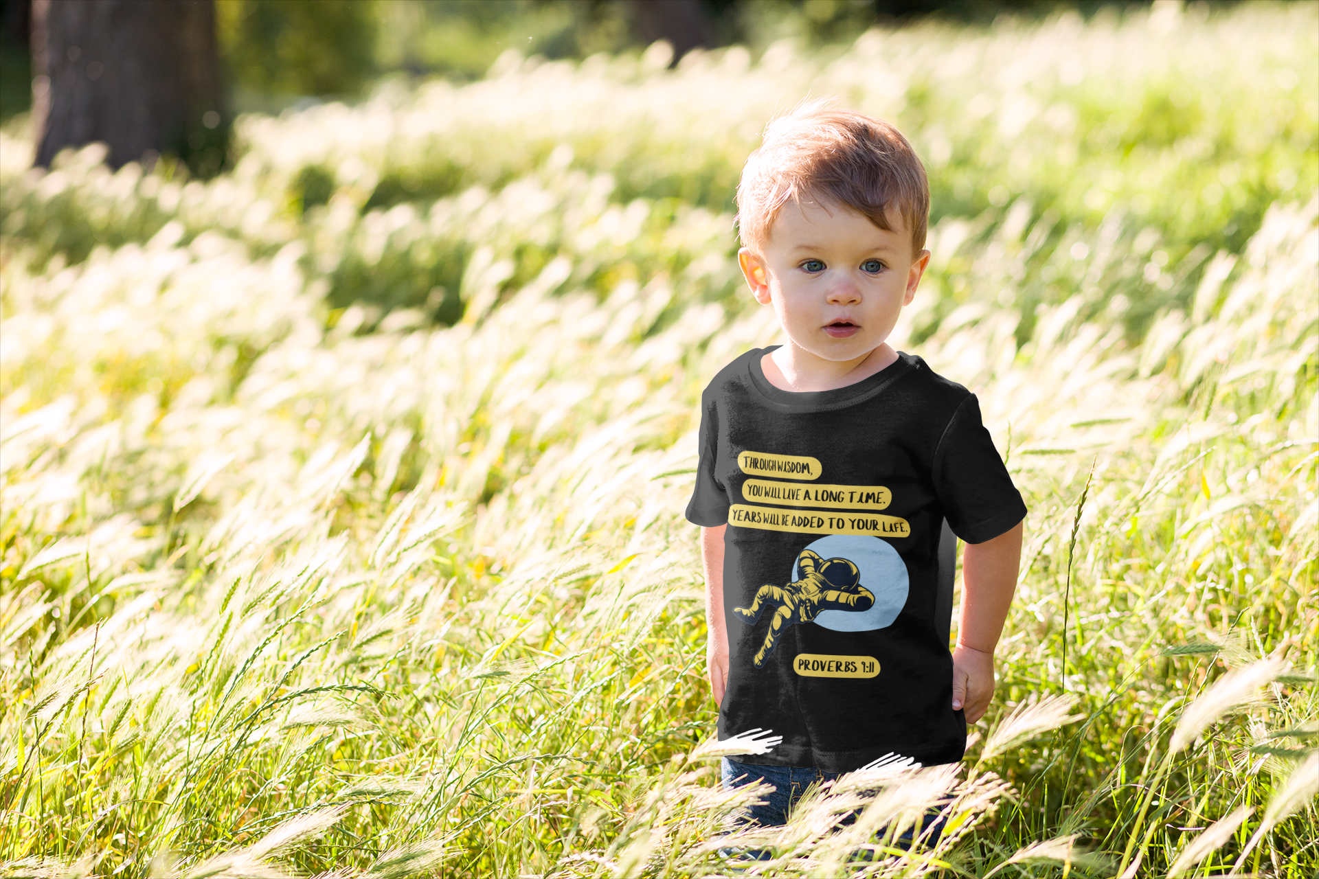 Child wearing a black t-shirt with Bible Verse and graphics in a grassy field