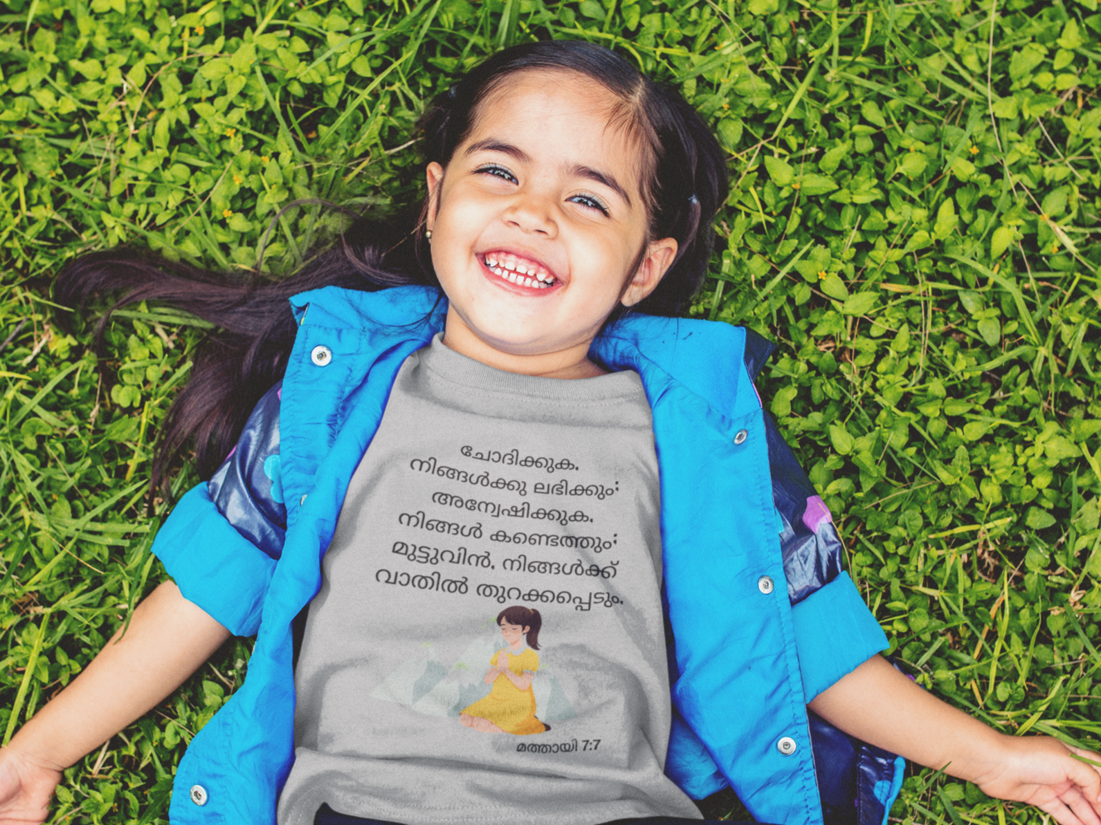 Child lying on grass wearing a blue jacket and gray shirt with text