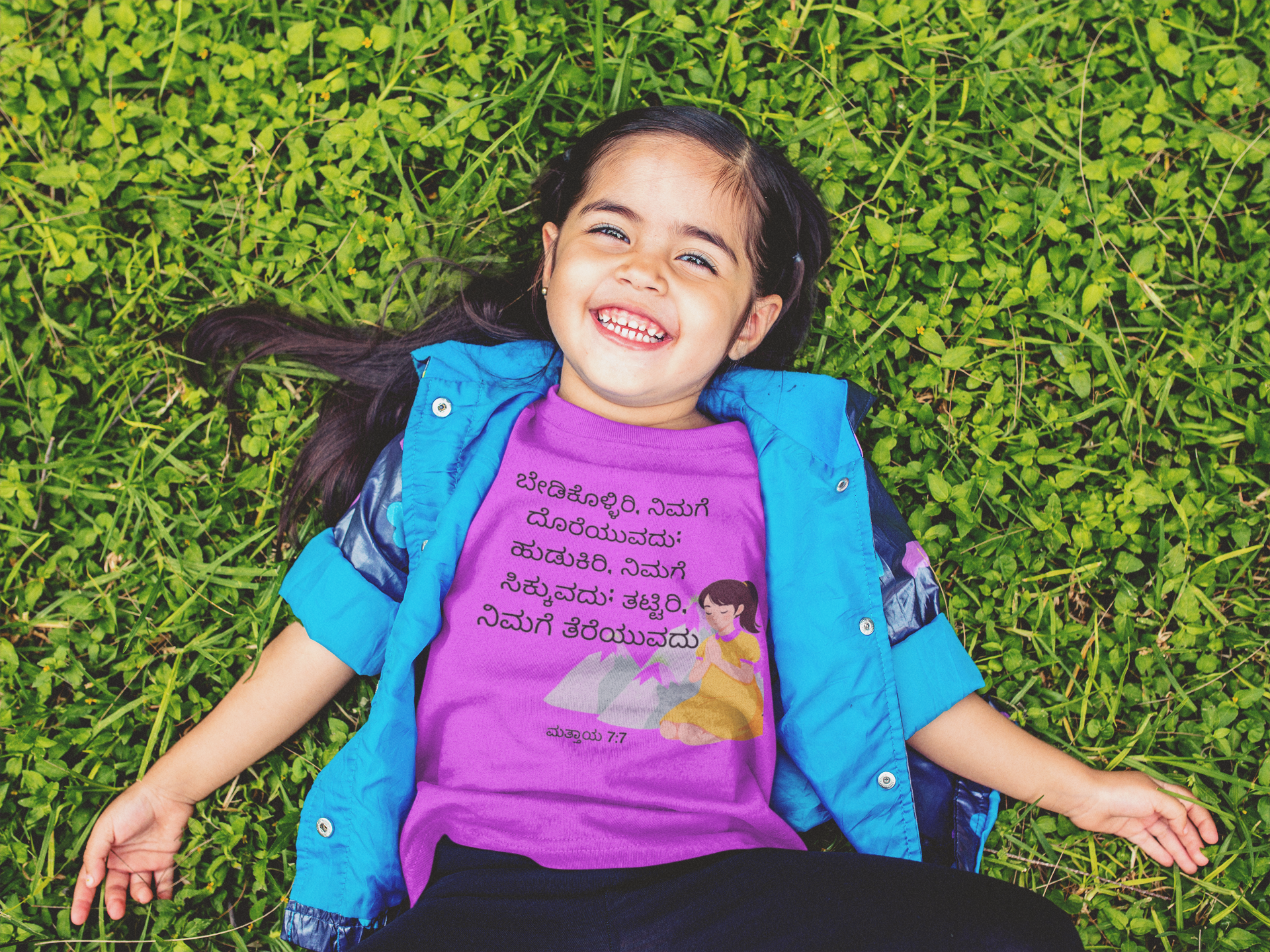 Child lying on grass wearing a purple shirt with text and graphics