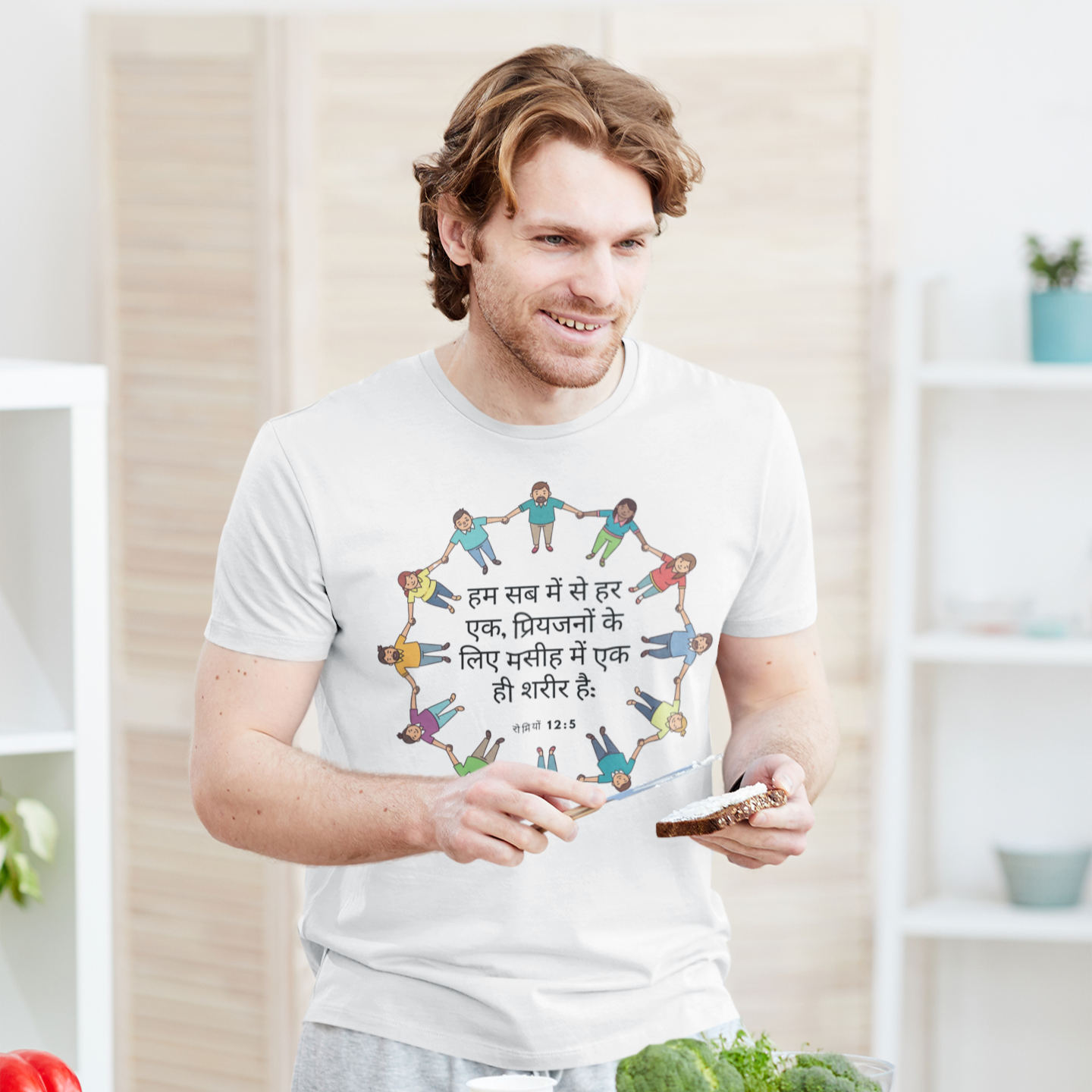 Man in a kitchen wearing a t-shirt with a colorful design, holding a phone.